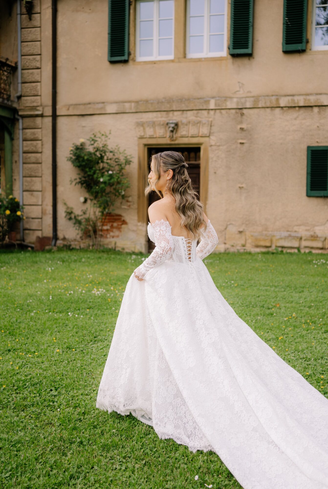 Braut im Spitzenkleid auf der Wiese vor dem Schlossgut