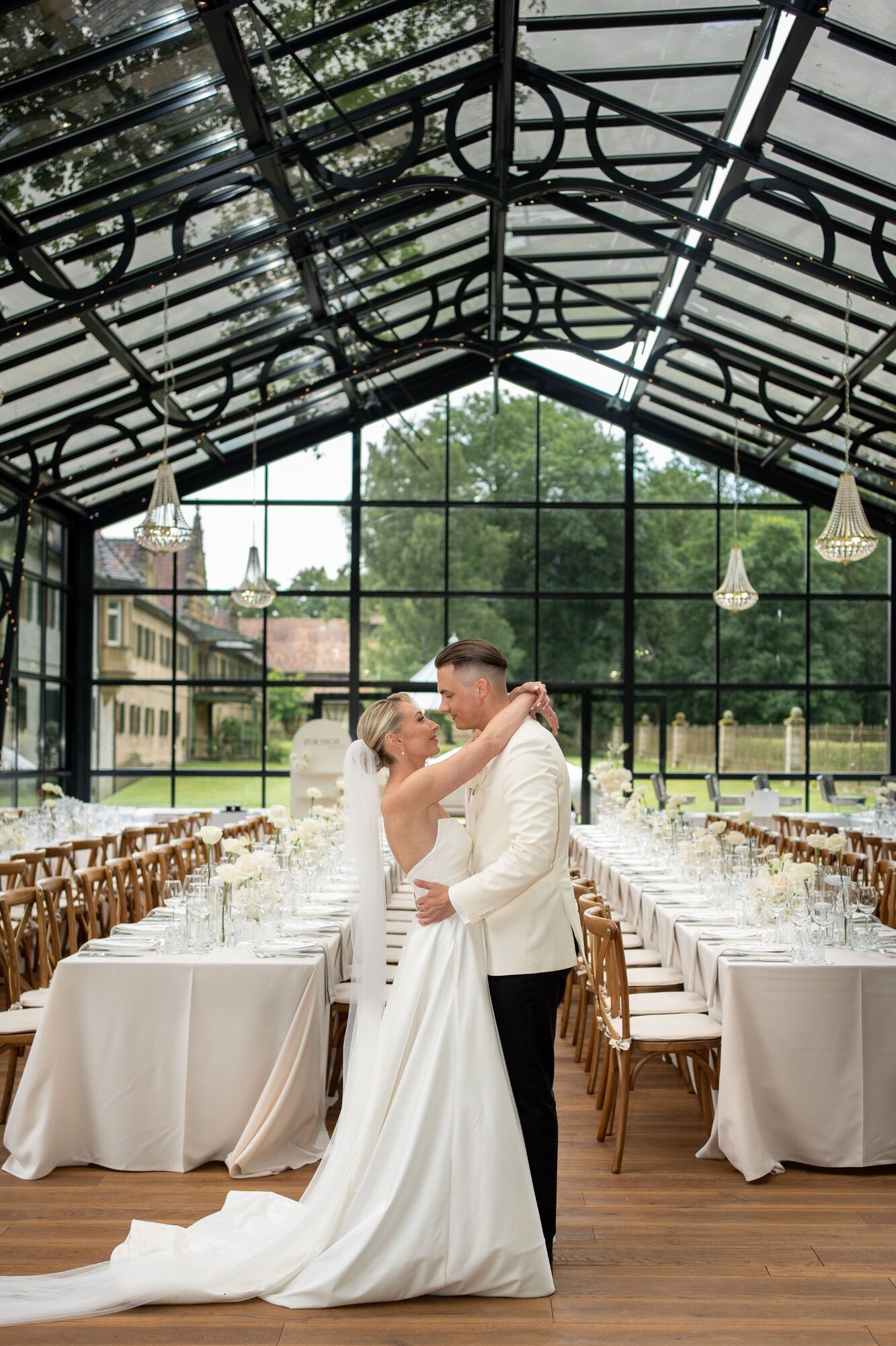 Hochzeitsfotograf Schlossgut Lautenbach – Brautpaar im Glaspavillon mit gedeckten Tischen.