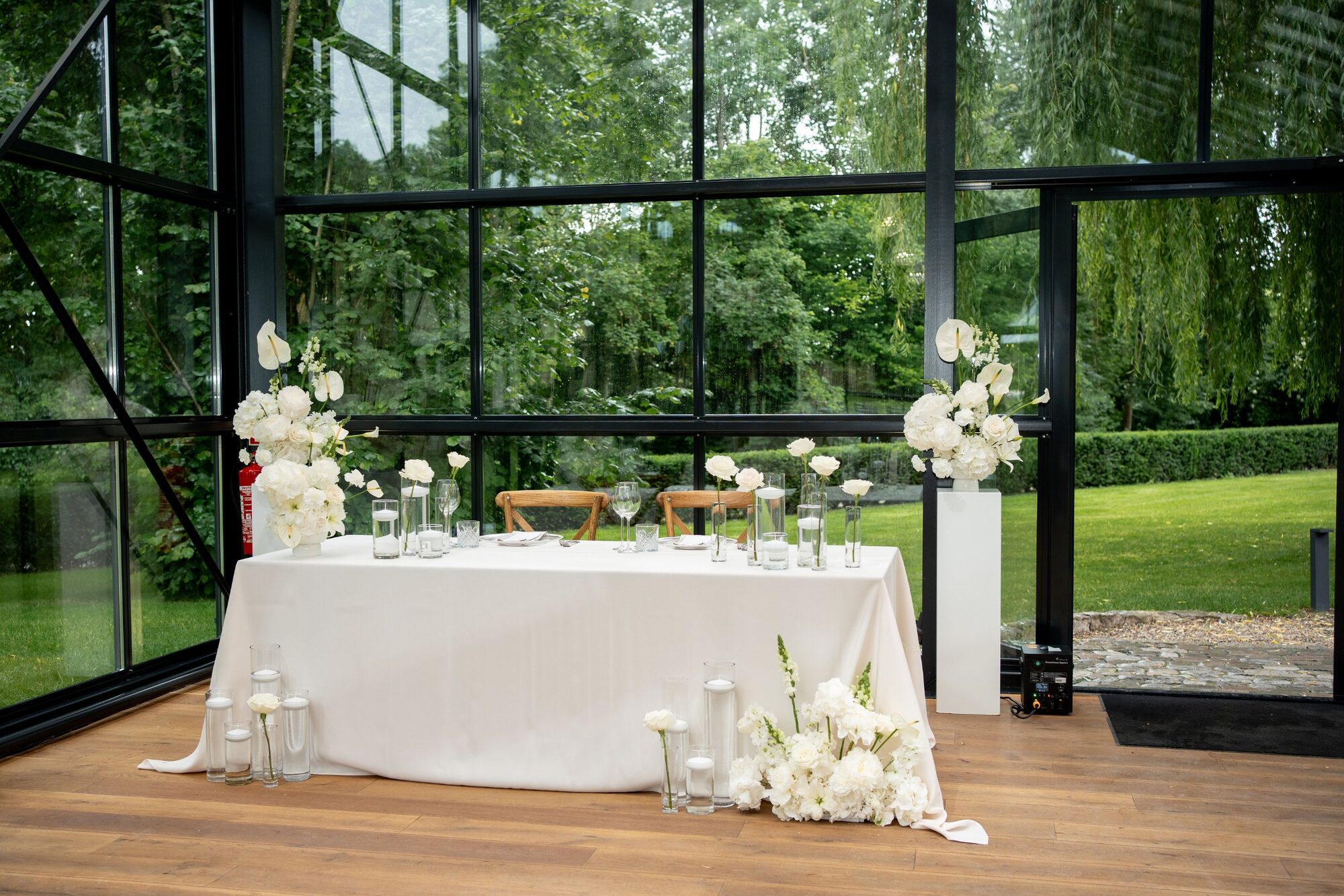 Brauttisch mit weißen Blumen im Glaspavillon